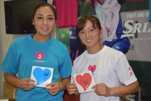 ご購入いただいたお客様にプレゼントする、サイン入りハートのシールを持ったディアス選手(左)と土居選手(右)