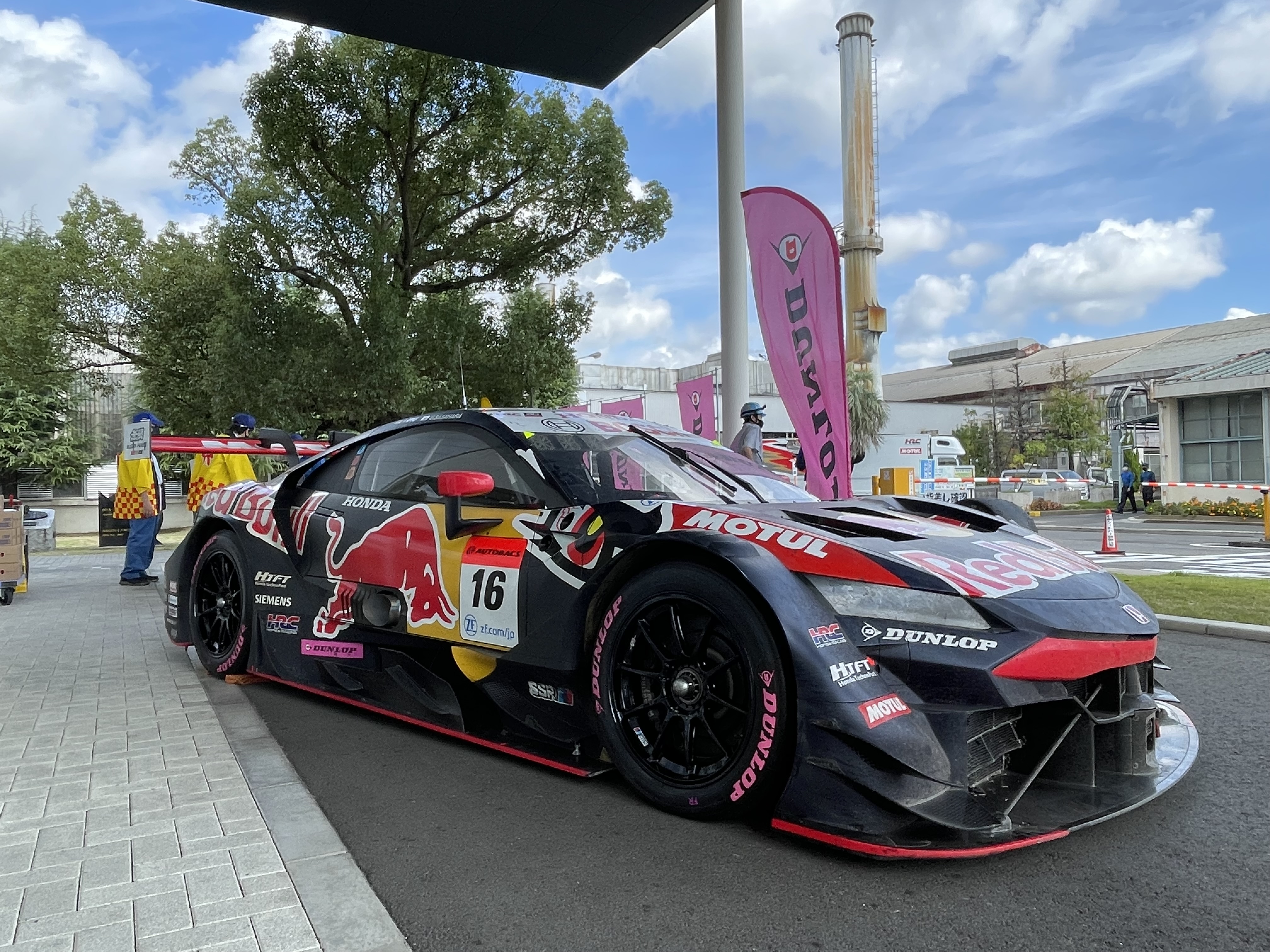A GT racing car, which has just finished racing, on display at the Nagoya Factory, with its tires bearing the pink DUNLOP logo.
